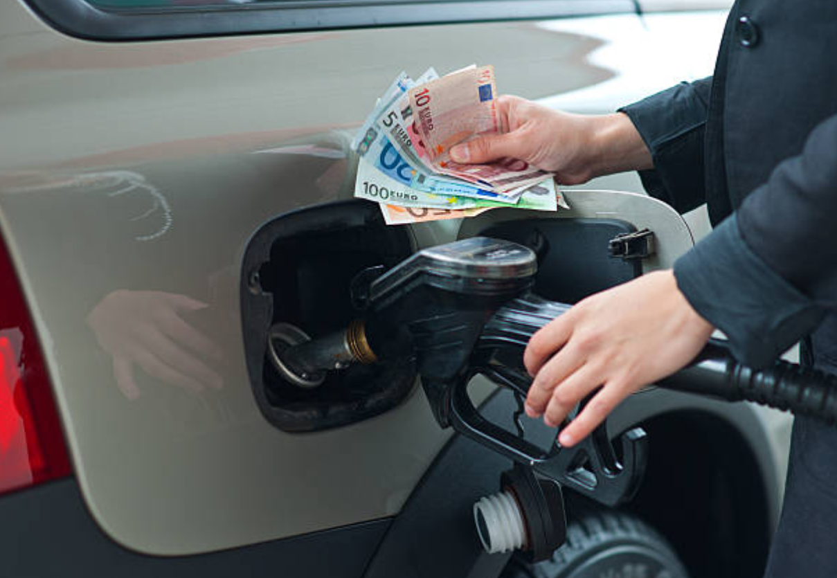 Automobiliste tenant des billets en euros pendant le plein de carburant à la pompe